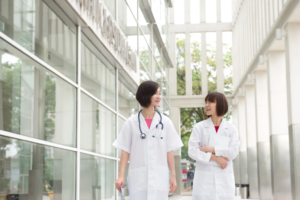 Two Doctors Walking Through Window-Filled Building Hallway